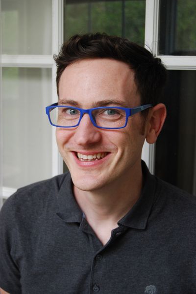 A picture of Michael, a white male with a slender build. He is clean-shaven, has auburn hair that is parted left to right and is wearing blue rimmed glasses and a dark grey polo shirt.